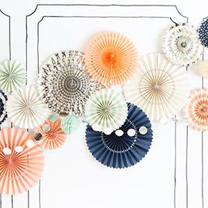 Navy, Peach, Blush Pink, Cream, and Mint paper party fans on a wall with a circle banner