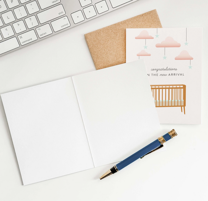 Greeting card with baby crib, clouds, star illustration on a desk with keyboard and pen