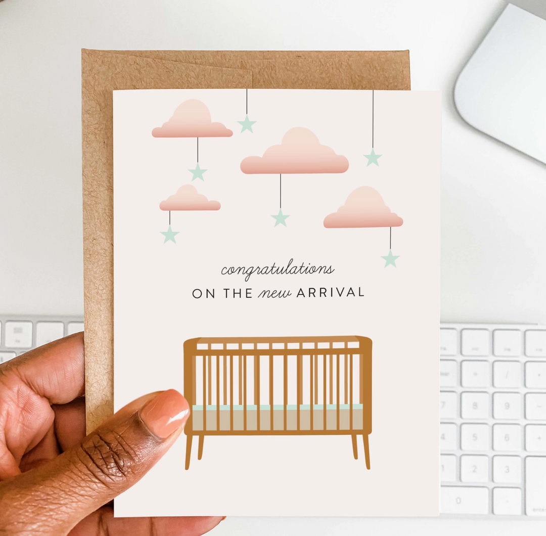 Greeting card with crib and cloud design held by a hand above a keyboard