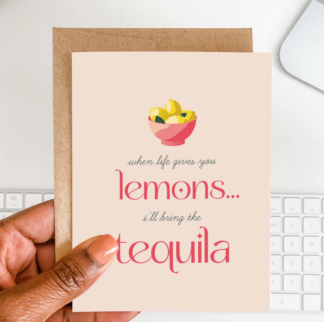 a hand holding a pink greeting card with an illustrated bowl of lemons and pink and green text that reads when life gives you lemons, i&