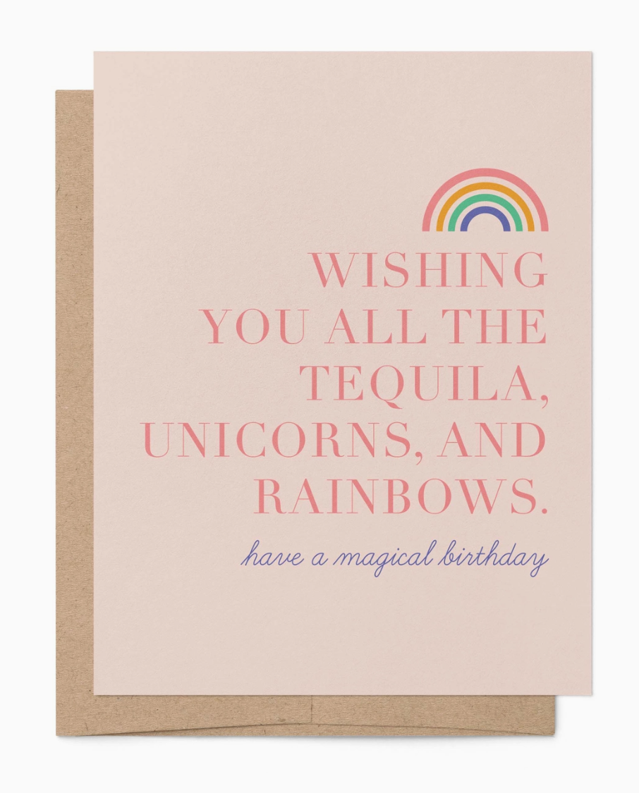 A pink greeting card with a rainbow sketch which reads "wishing you all the tequila, unicorns, and rainbows. have a magical birthday" with a brown envelope