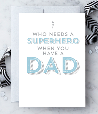 A white greeting card with grey and blue text that reads 'Who needs a Superhero when you have a dad". Paired with a silver envelope.