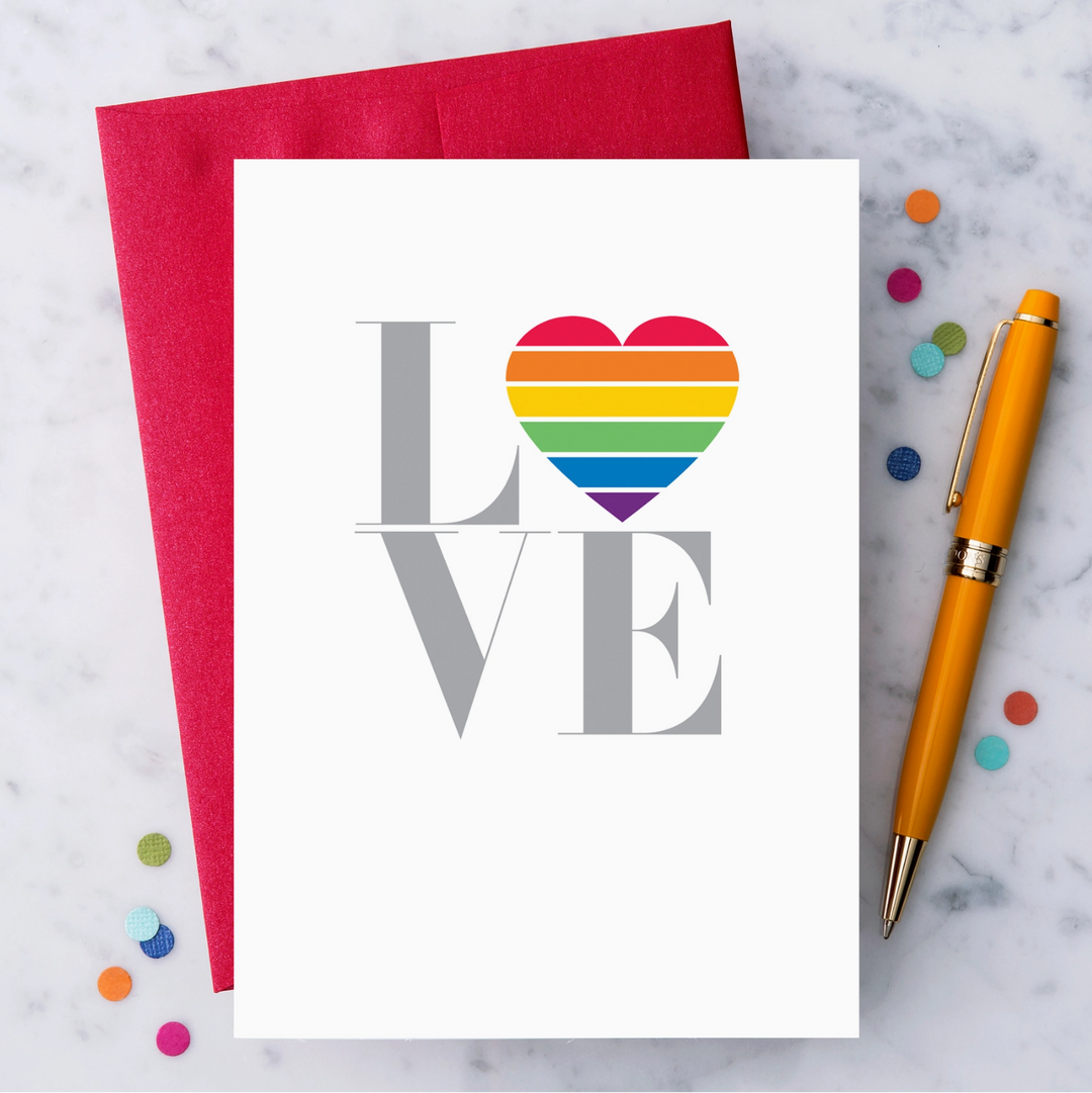 A white greeting card featuring the word "LOVE", the letters L, V, and E are in metallic silver and the letter O is replaced with a rainbow striped heart. Paired with a metallic red envelope.