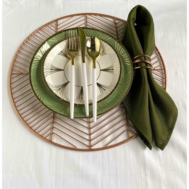top view of a table setting, rose gold wire placemat topped with stack of a sage green and gold art deco inspired printed dinner plate, a white and gold art deco inspired printed salad plate, white handled gold utensil set, and a green folded napkin with rose gold napkin ring