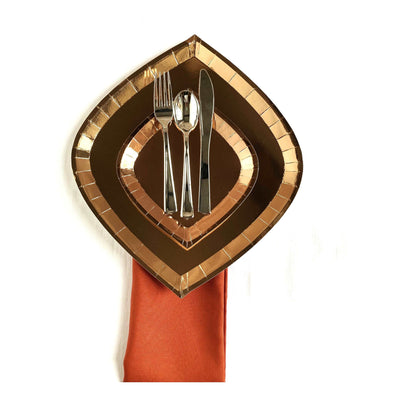 orange napkin with rose gold foil charger plate and dessert plate on top,  topped with a 3 piece silver flatware set against a white background