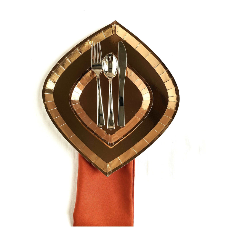orange napkin with rose gold foil charger plate and dessert plate on top,  topped with a 3 piece silver flatware set against a white background