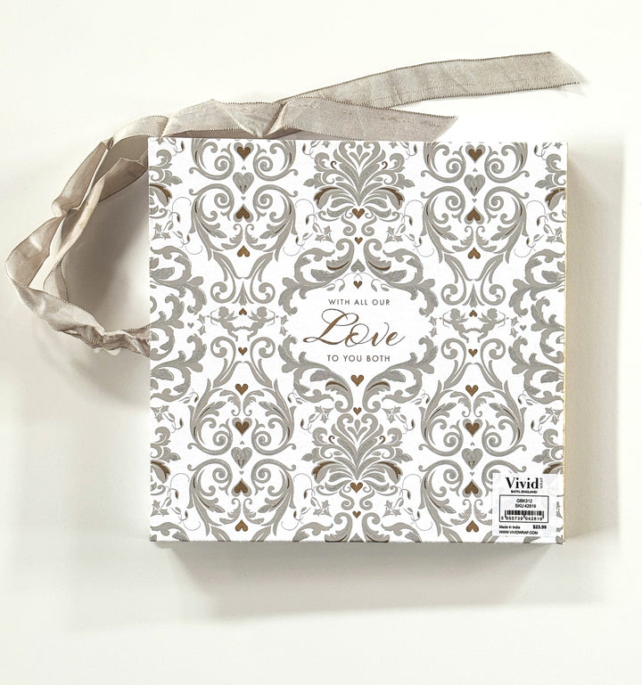 White book with screen-printed baroque style pattern in grey and gold. The words with all our love to you both in gold in center of book, grey ribbon wrapped from the side to the top