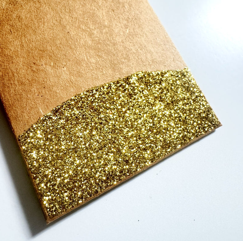 Close up of a kraft paper gift tag with the bottom dipped in gold glitter