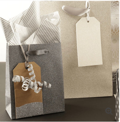 Silver gift bag with silver and white striped tissue paper coming out of the top. kraft paper gift tag dipped in silver glitter hanging on the front of bag