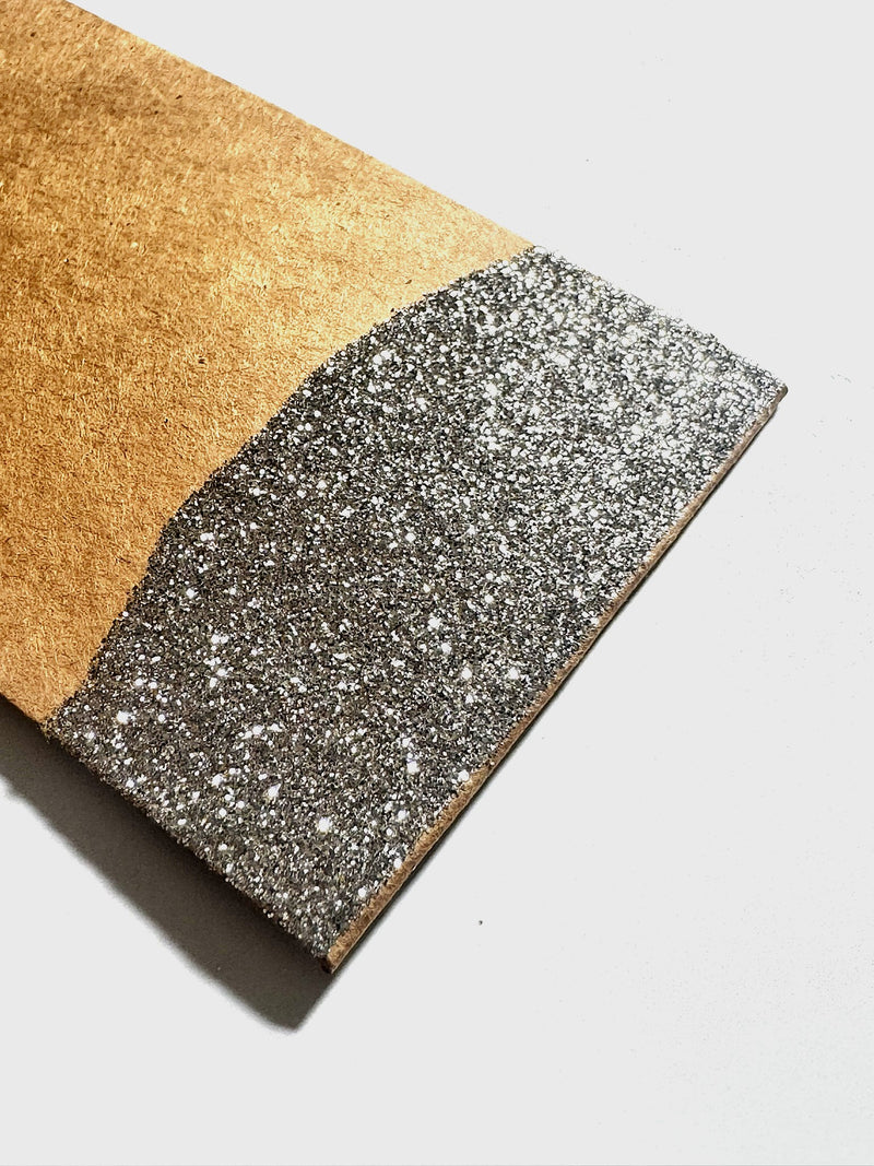 Close up of a kraft paper gift tag with the bottom dipped in gold glitter