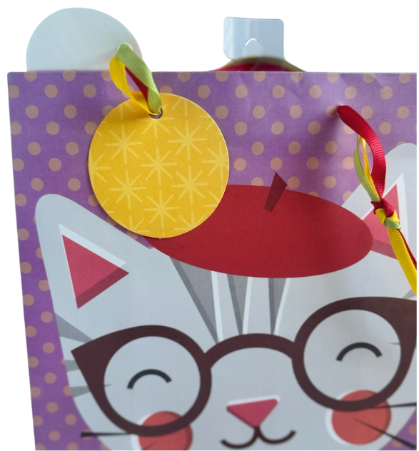 Purple gift bag with yellow polka dots and a smiling kitten wearing a red beret hat, glasses, and a cozy orange sweater. Multi-strand ribbon handles in red, yellow, and green and yellow gift tag