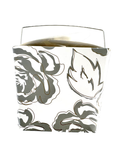 A close-up image of a white take-out style box with an allover silver and gold floral pattern.