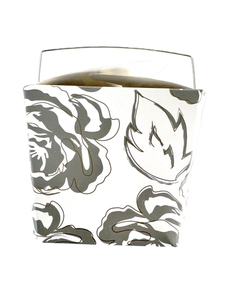 A close-up image of a white take-out style box with an allover silver and gold floral pattern.
