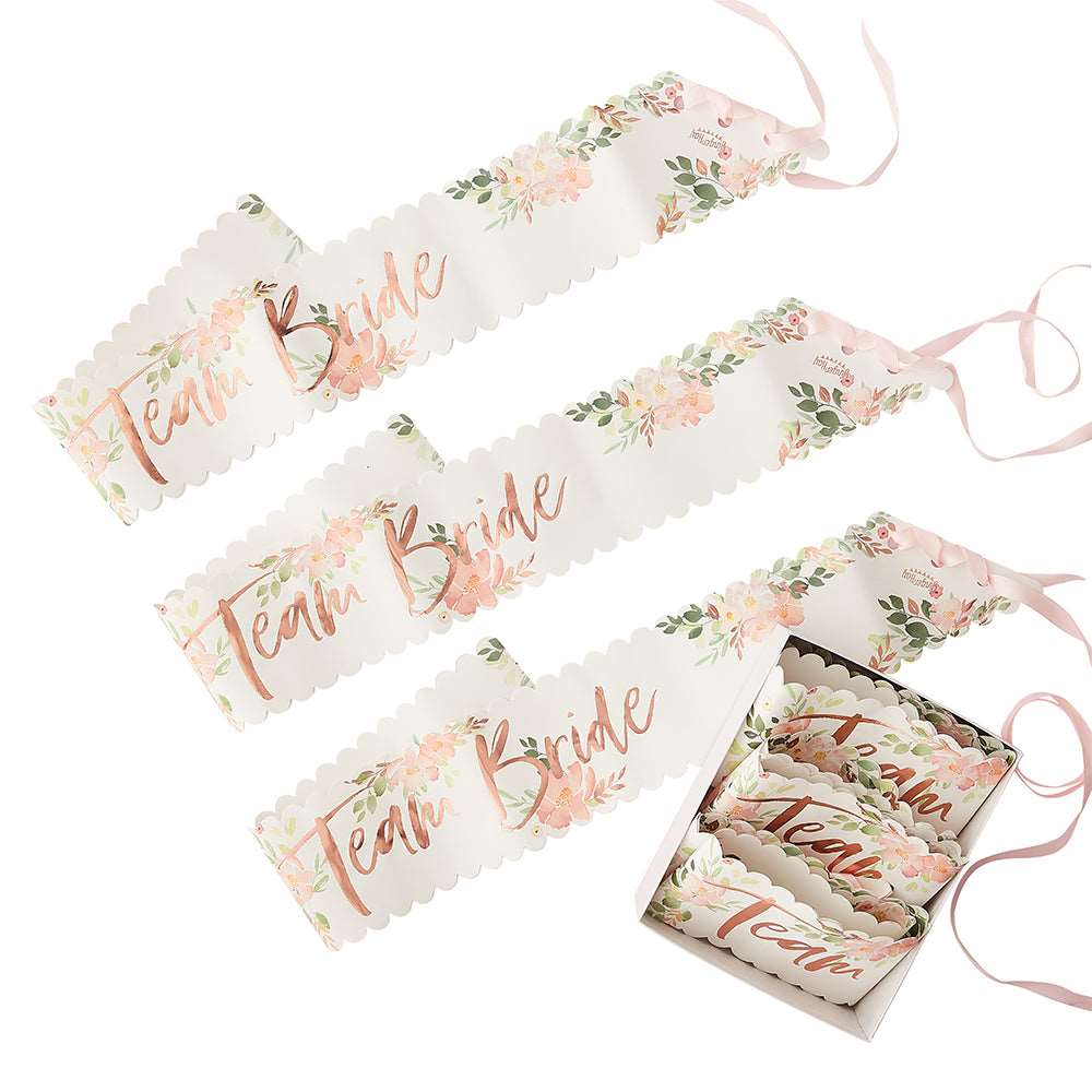 Three paper sashes with floral patterns and 'Team Bride' printed in rose gold foil, tied with pink ribbons.