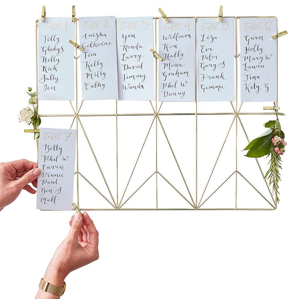 A gold wire frame on which table number cards are displayed, with the numbers 1 to 12, accompanied by small gold clothes pins for mounting.