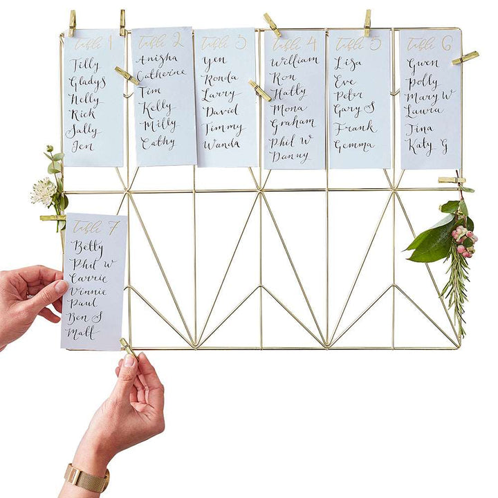 A gold wire frame on which table number cards are displayed, with the numbers 1 to 12, accompanied by small gold clothes pins for mounting.
