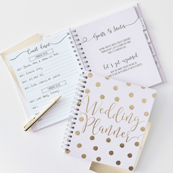 An open pale lavender spiral notebook  with wedding planning details listed, along with a gold pen.