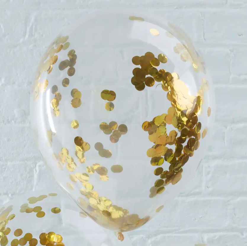 Clear balloon with gold confetti against a white brick wall