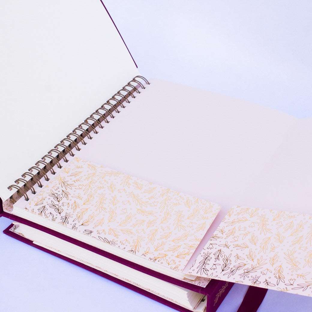 A wine-burgundy fabric-covered wedding planner book open to pocket folders on a white background