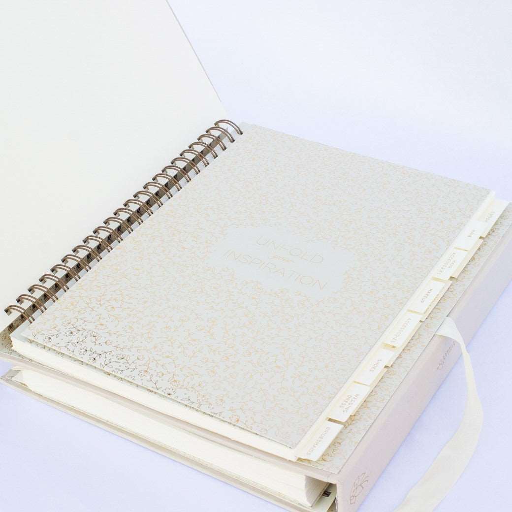 A beige fabric-covered wedding planner book open to the inspiration section cover page on a white background