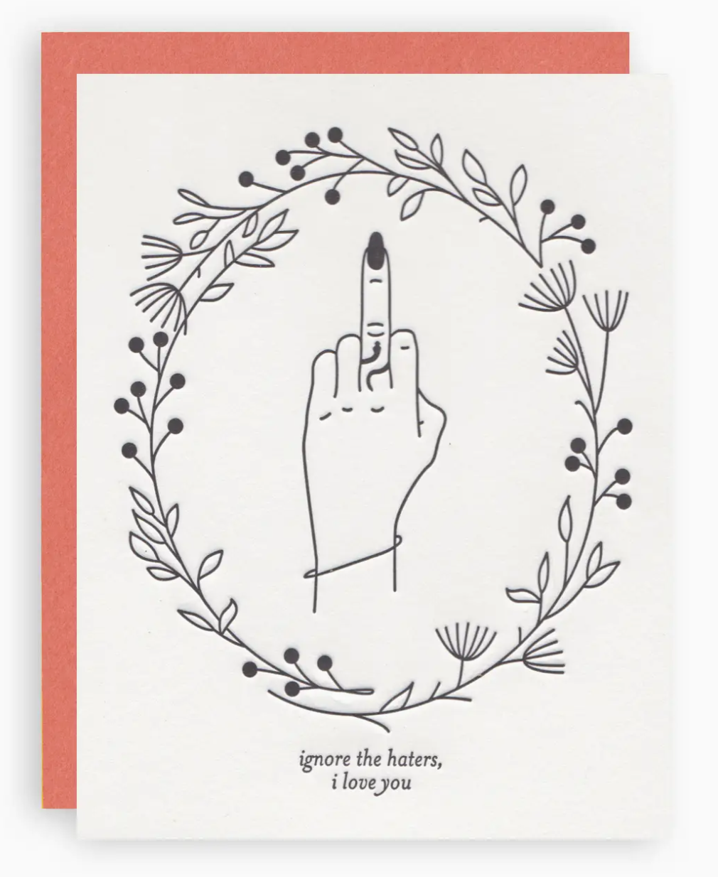 White greeting card with an illustration of a wreath and a hand with the middle finger extended in the middle of the wreath and black text that reads "Ignore the haters, i love you" below wreath. Paired with a pumpkin-orange colored envelope.