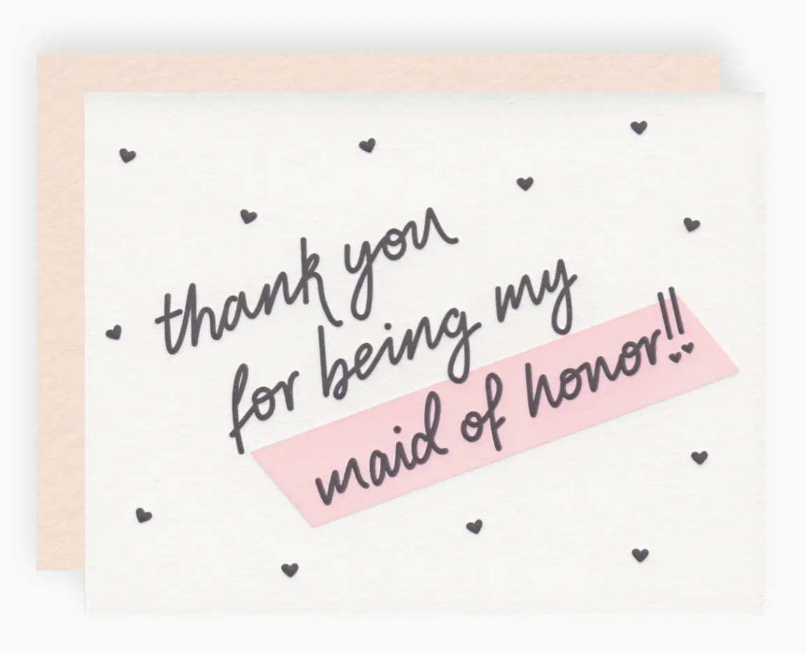 White greeting card with black mini hearts printed allover and text that reads "thank you for being my maid of honor!!" paired with a blush pink envelope