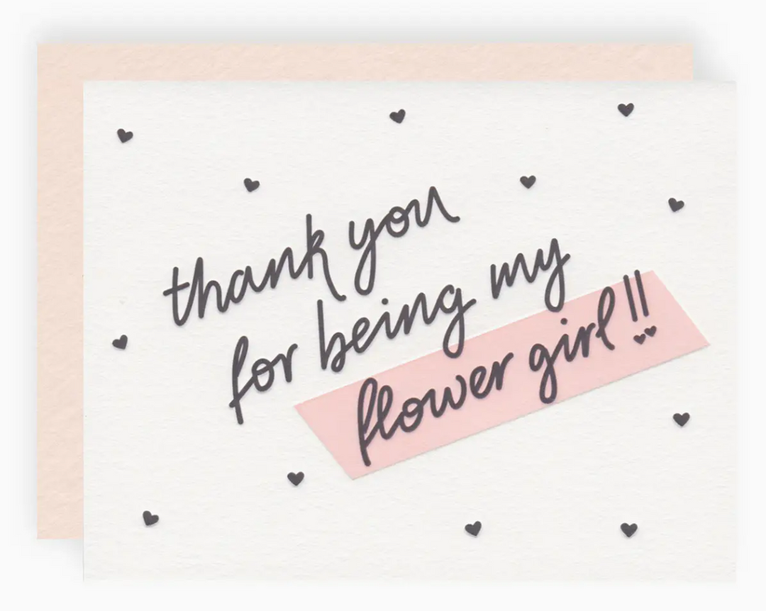 White greeting card with black mini hearts printed allover and text that reads "thank you for being my flower girl!!" paired with a blush pink envelope