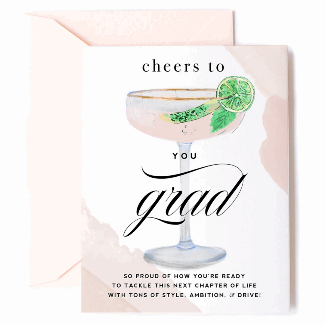Greeting card with an illustrated filled gold-rimmed coupe-style glass with mint leaf and lime slice on the rim and caption that reads "Cheers to YOU Grad. So proud of how you&