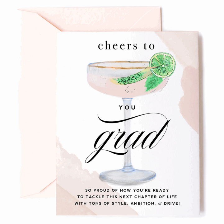 Greeting card with an illustrated filled gold-rimmed coupe-style glass with mint leaf and lime slice on the rim and caption that reads "Cheers to YOU Grad. So proud of how you&