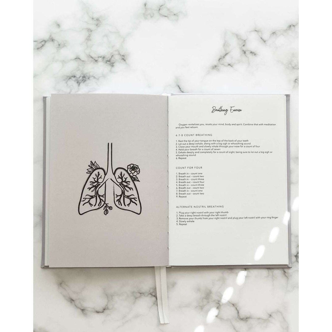 A journal opened to a page that has a sketch of a pair of lungs surrounded by flowers and another page that lists types of breathing exercises on top of a marble table.