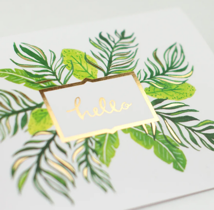 White greeting card with gold foil outlined square with the text "hello" in gold foil and illustrated green and gold palm and fern design coming out from behind the square from all sides