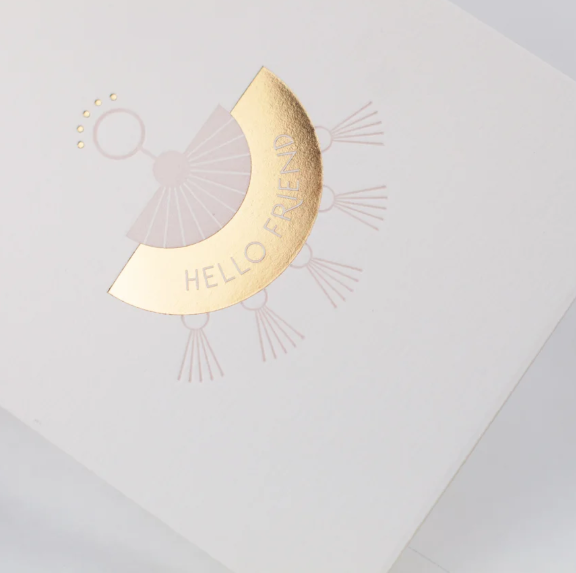 White greeting card, with a pink and gold foil letterpress tassel style earring with the text "Hello Friend"