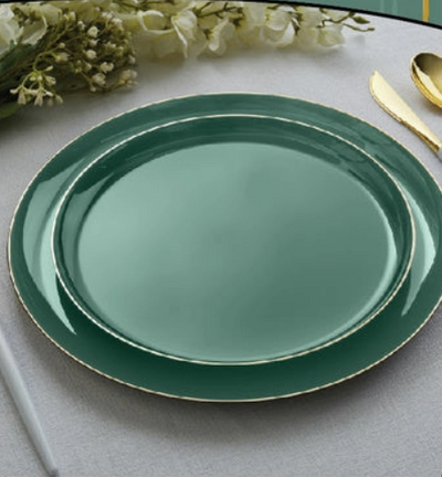 Green dinner and salad plates with gold rim on a light gray surface with flowers and a spoon.