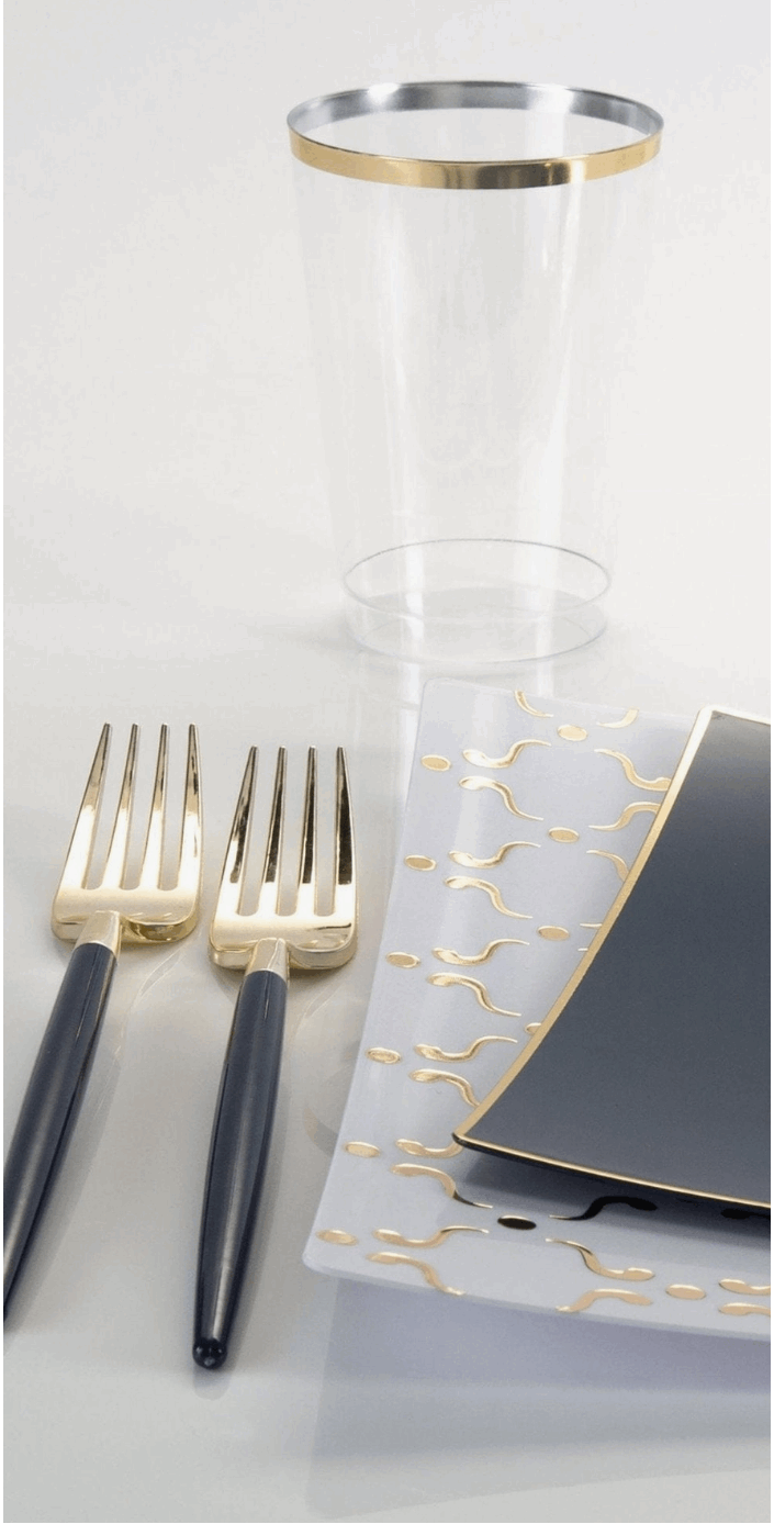 2 black handled forks next to a white with gold printed square plate topped with a black with gold rim square salad plate and a clear plastic cup with gold rim