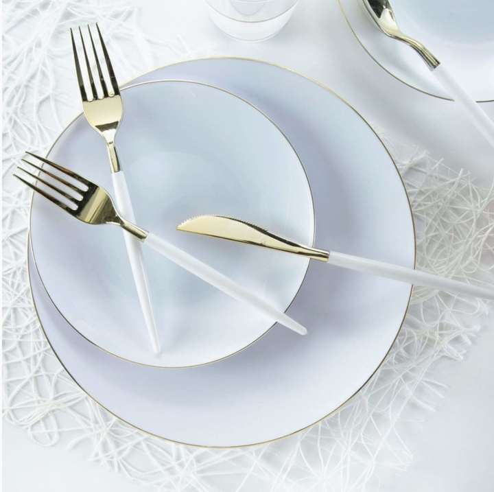 White dinnerware set with gold rims and white and gold cutlery on a textured white surface
