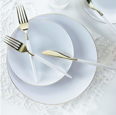 White dinnerware set with gold rims and white and gold cutlery on a textured white surface