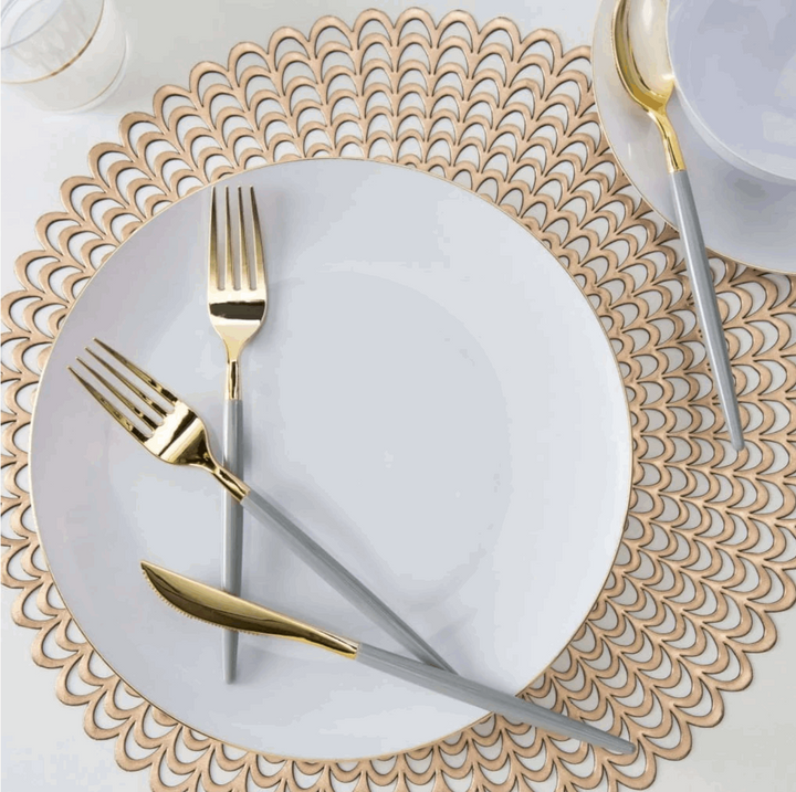 White tableGrey and Gold Plastic Cutlery Set-32pcwith gold placemat topped iwth a white and gold rimmed plate with grey-handled and gold knife and 2 forks on top. white with gold rim salad plate and bowl with grey-handled and gold spoon and a clear cup with gold rim next to everything