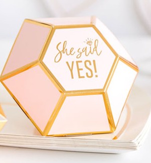 A diamond-shaped die-cut pink favor box with gold foil trim detail and gold foil print that reads "she said yes" in the center. 