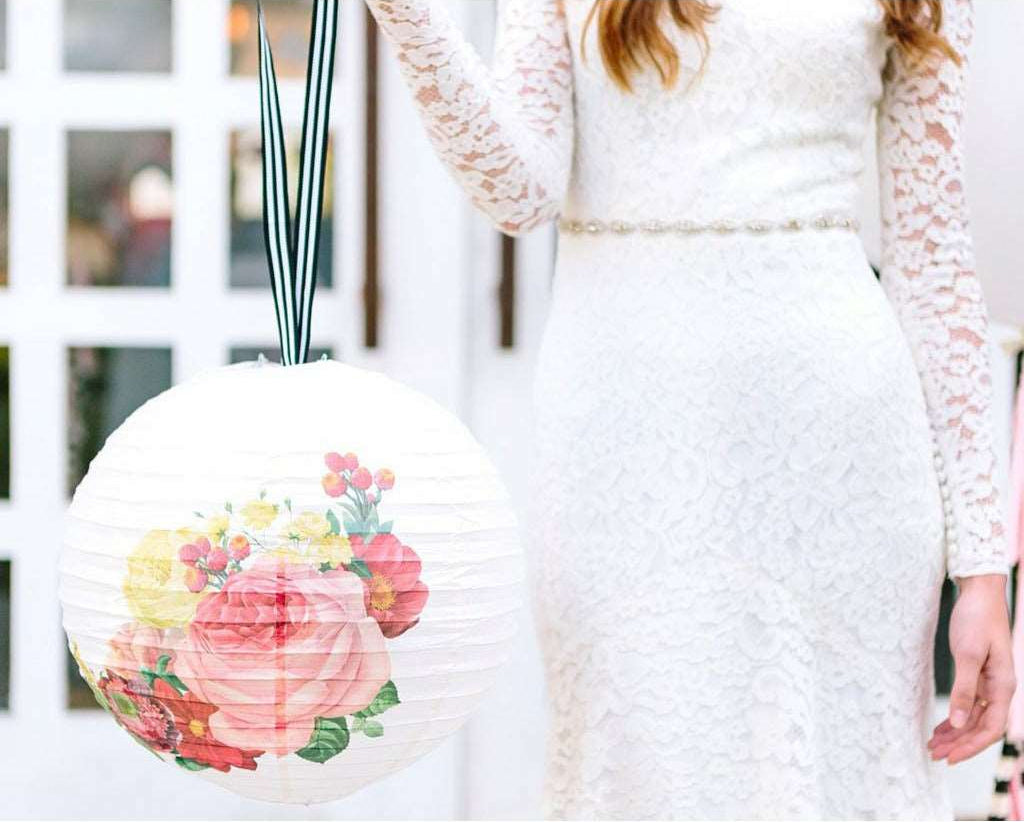 Decorative paper lantern with floral print design and black and white striped ribbon hanger against a blurred indoor background