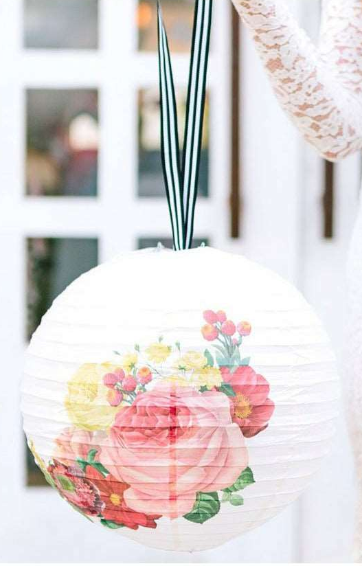 Decorative paper lantern with floral print design and black and white striped ribbon hanger against a blurred indoor background