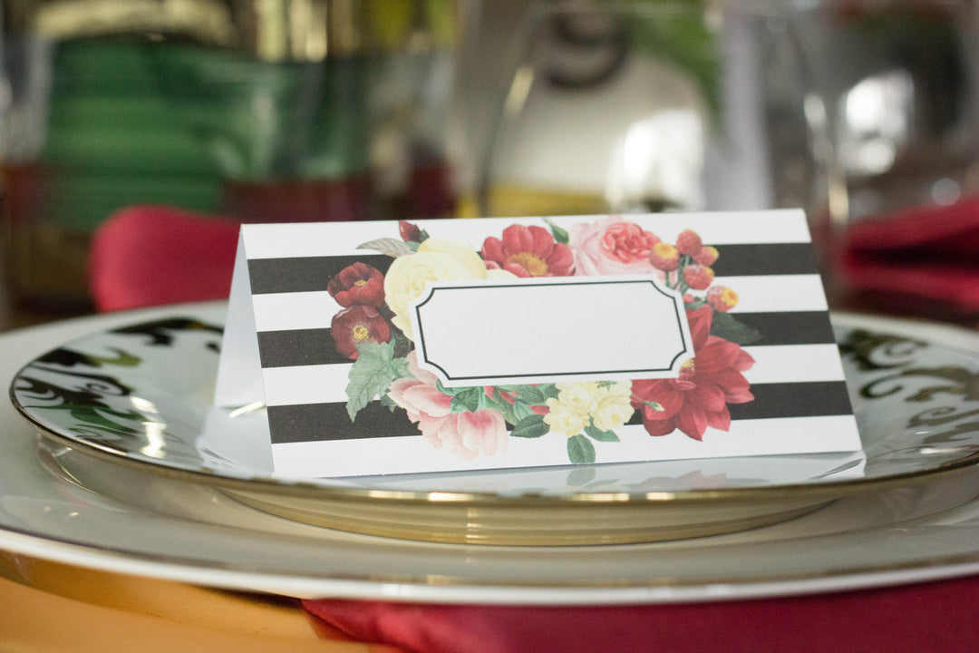 black and white striped place cards with a multi-color floral print surrounding space for names on top of a white with gold trim dinner plate.
