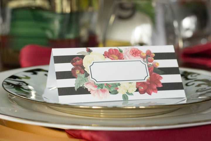 black and white striped place cards with a multi-color floral print surrounding space for names on top of a white with gold trim dinner plate.