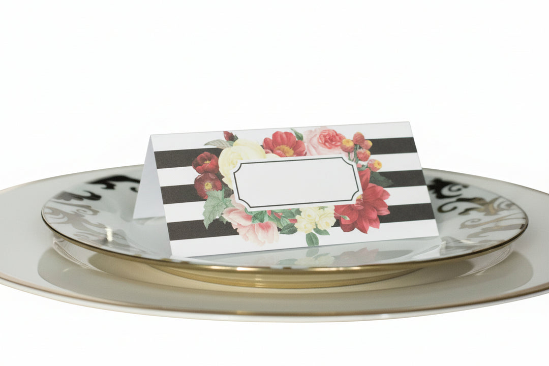 black and white striped place cards with a multi-color floral print surrounding space for names on top of a white with gold trim dinner plate.