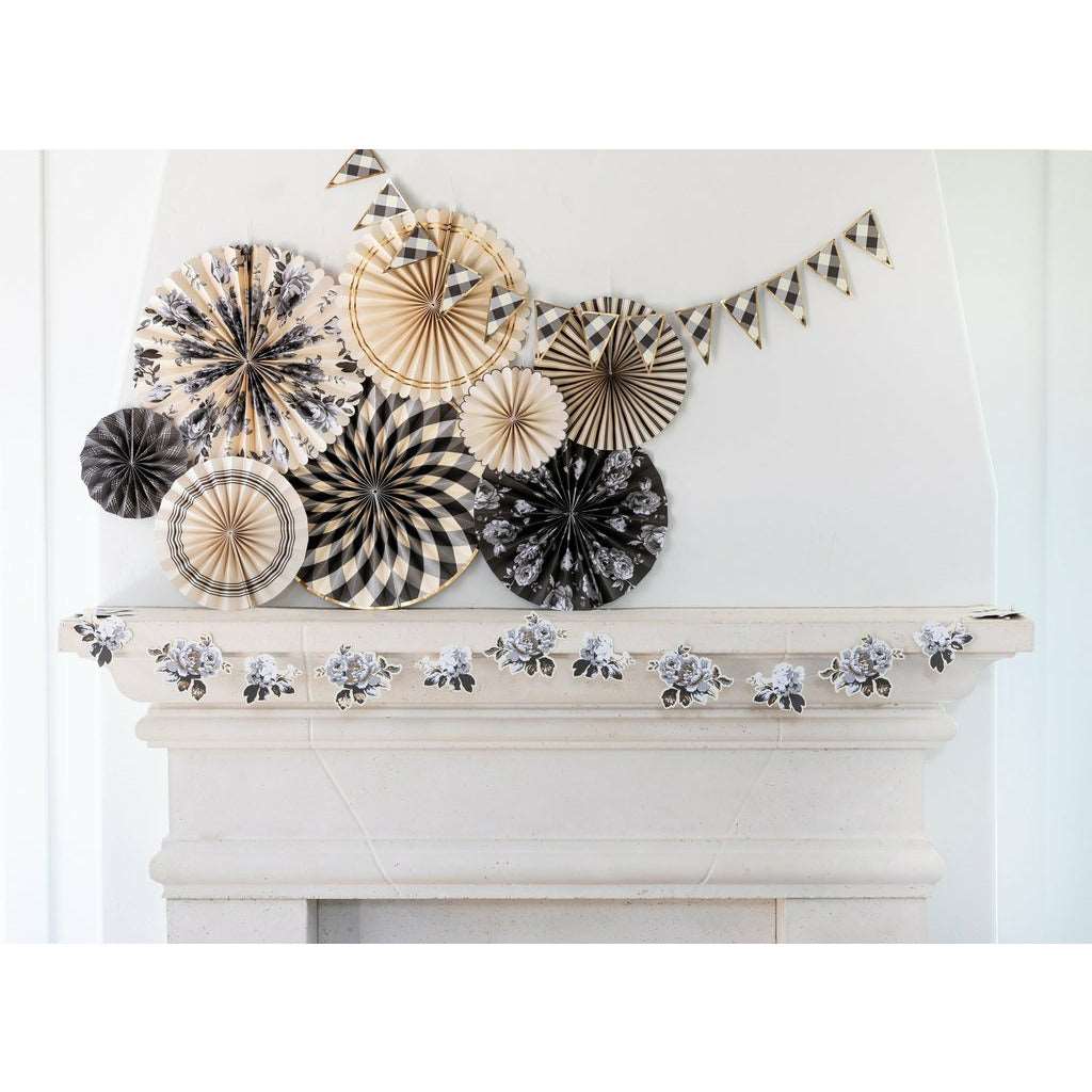 white stone fireplace with die-cut grey and white flower banner draped on the front mantel, black, white and gold gingham printed pennat banner hung on the chimney along with black, white and gold party fans in different sizes and patterns.