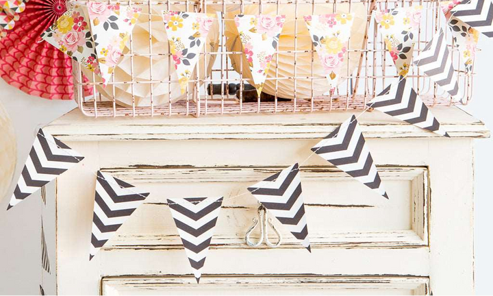 2 Pennant-style banners, 1 with a black and white chevron print banner and 1 with a multi-floral print on a white wood dresser