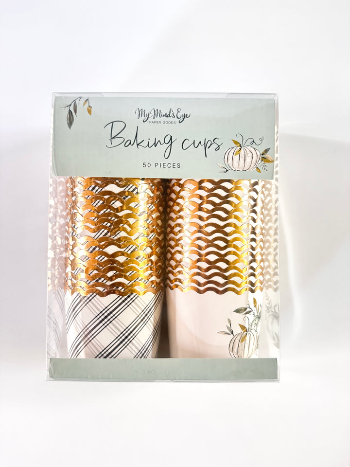 Picture of a package of a black and white plaid printed baking cup with gold foil rim and a white gold foil rimmed backing cup with 2 green, black, and gold printed pumpkins and foliage.