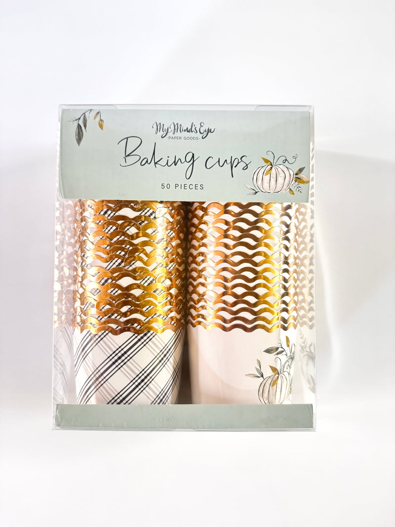 Picture of a package of a black and white plaid printed baking cup with gold foil rim and a white gold foil rimmed backing cup with 2 green, black, and gold printed pumpkins and foliage.