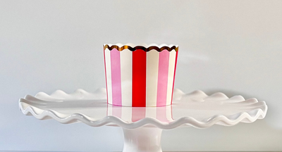Red, pink, and white striped baking cup with gold foil printed top edge on a white cake platter