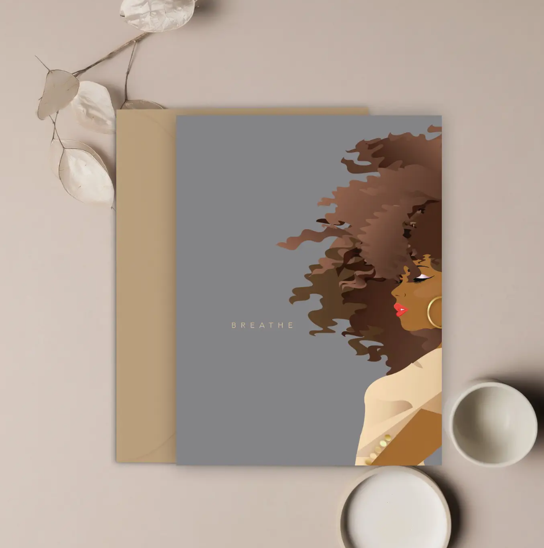 A greeting card with a illustration of a woman's side profile in brown tones, with the word 'BREATHE' in capital letters. It is placed on a beige background with a kraft brown envelope and some decorative elements to the side.