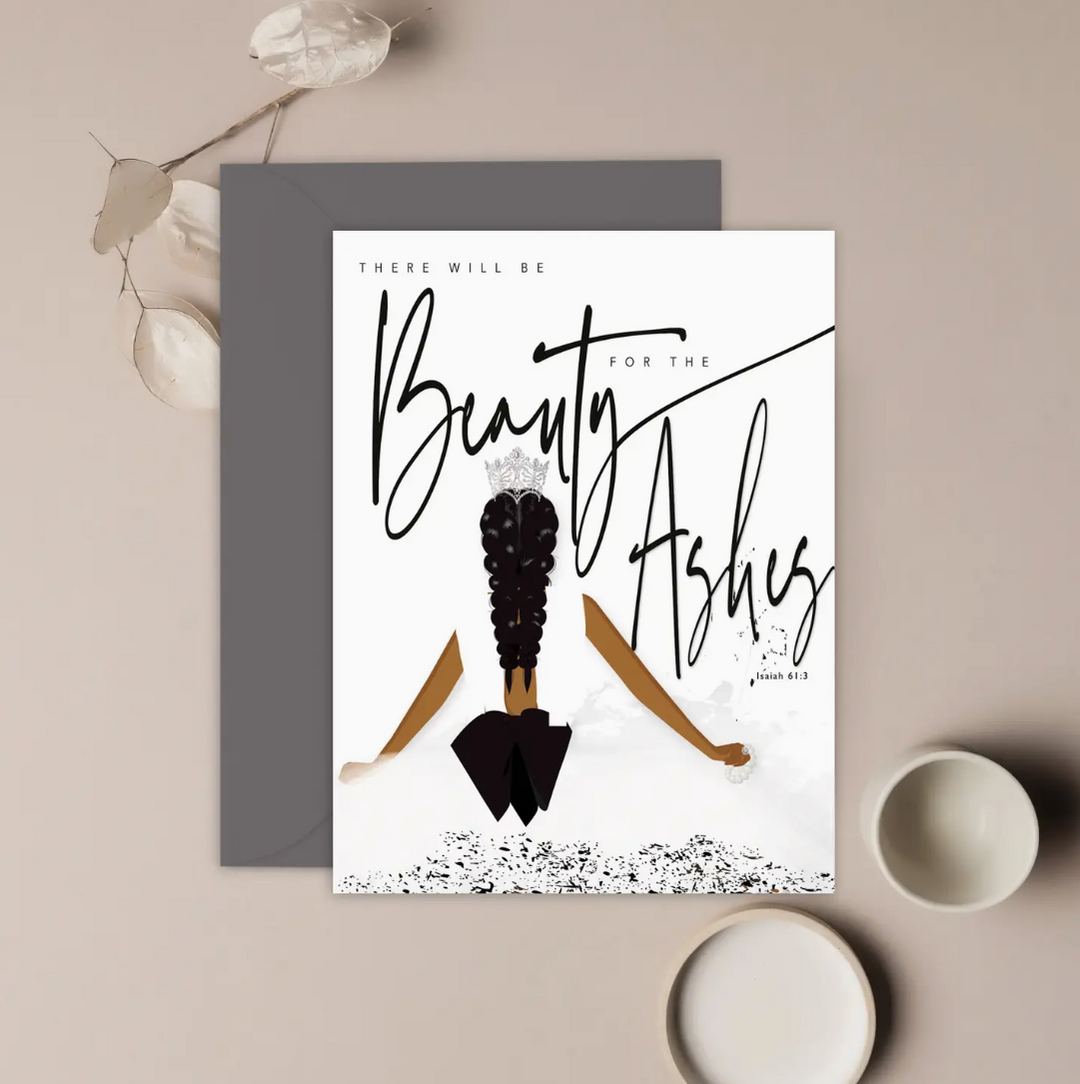 A white greeting card with an illustration of the back of a woman with a crown on her head, and text that reads there will be beauty for the Ashes, Isaiah 61:3. with a sage green envelope displayed on a neutral background.